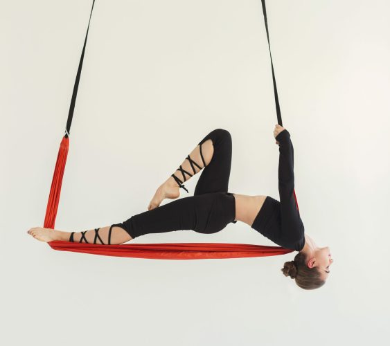Young slim woman practicing fly yoga asana and stretching over white background in fitness gym, copy space. Health, sport, yoga concept