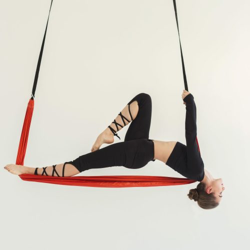 Young slim woman practicing fly yoga asana and stretching over white background in fitness gym, copy space. Health, sport, yoga concept