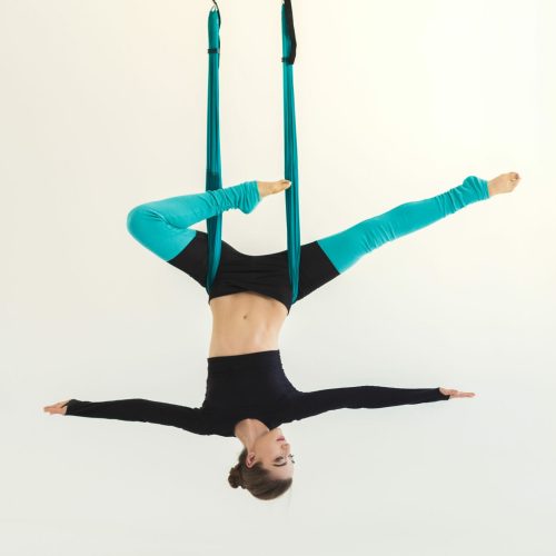 Happy woman practicing fly yoga asana over white background in fitness studio, copy space. Health, sport, yoga concept