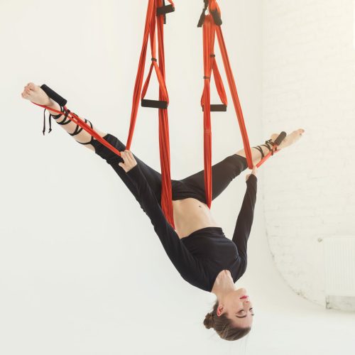 Caucasian woman practicing fly yoga asana, hanging head down over white background in fitness gym, copy space. Health, sport, yoga concept